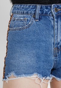 Denimshorts i ljusblått med fransad nederkant, med en sidodetalj i leopardmönster. Inkluderar vanliga fram- och bakfickor.