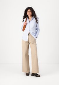 Camasa cu dungi albastre și albe, pantaloni largi bej, pantofi din piele maro și o geantă de umăr maro. Ținută simplă și casuală.