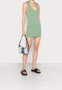 Zelené žebrované mini šaty s ramínky, kombinované s černou a mátovou taškou se vzorem a černými plochými sandály se zlatými akcenty.