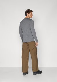 Chemise grise à manches longues associée à un pantalon cargo marron ample. Le pantalon possède une poche latérale et un détail de cordon de serrage. Des chaussures noires complètent le look.