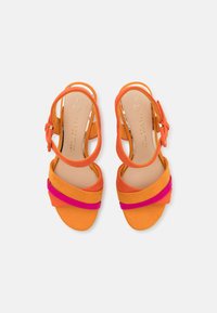Sandales à talons ouverts avec des brides en faux suede orange et rose. Elles disposent d'une fermeture par boucle et d'une semelle intérieure beige lisse avec un logo embossé.