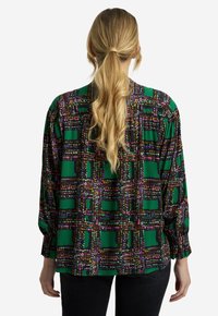 Blusa a maniche lunghe in tessuto verde con motivo geometrico multicolore. Caratterizzata da una vestibilità ampia e maniche arricciate con orlo arrotondato.