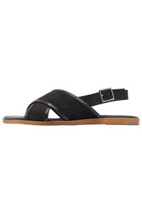 Black suede sandals featuring crisscross straps, a minimalist design, and an adjustable buckle. The sole is flat with a wooden finish.
