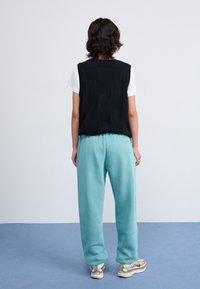 Haut sans manches noir avec un motif de grille texturé, associé à un pantalon de survêtement bleu ciel et des baskets avec des accents dorés. Design minimaliste.