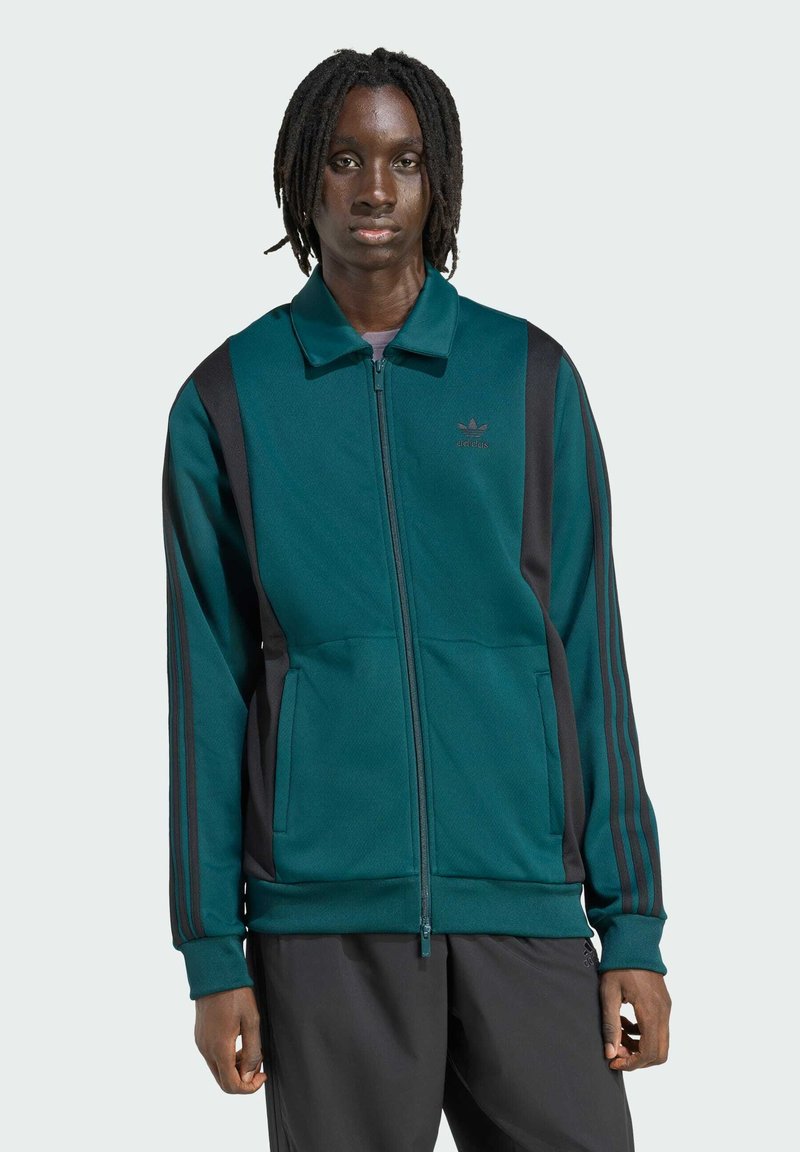 Teal zip-up jakke med sorte sidepaneler og tre sorte striber på ærmerne. Har krave og frontlommer.