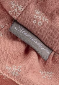 Tessuto rosa con una trama testurizzata, decorato con motivi floreali bianchi. Include un'etichetta grigia con il nome "Sterntaler" ricamato in bianco.