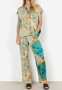 Zwei-teiliger Anzug bestehend aus einem kurzärmligen, kragenlosen Hemd und weit geschnittenen Hosen in Teal, Gelb und Beige mit Blattmustern und abstrakten Designs.