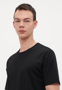 T-shirt nera realizzata in misto cotone, con scollatura a girocollo e maniche corte, dalla texture liscia e design aderente.