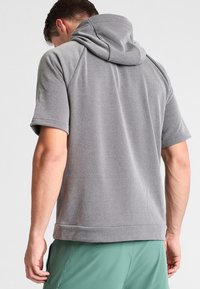 Sweat à capuche gris à manches courtes, texture douce et capuche avec cordon de serrage. Présente une coupe décontractée et un ourlet, vu de dos.