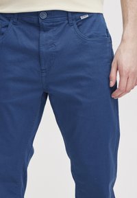 Niebieskie spodnie z bawełnianego materiału w prostym kroju, z przodem zapinanym na guzik, dwiema bocznymi kieszeniami i delikatną teksturą.