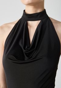 Musta halterneck-toppi, jossa on laskostettu etuosa, sileä pinta ja tiukka siluetti, korostaen virtaviivaista ja minimalistista muotoilua.