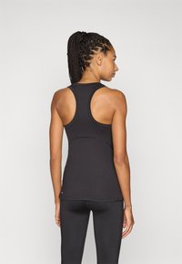 Crni sportski top s racerback dizajnom, prilagodljiv oblik, glatka tekstura i šivani detalji, uparen s crnim tajicama.