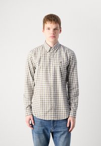 Camicia a maniche lunghe con motivo a quadretti marroni e bianchi, con colletto button-down e patta frontale, indossata sopra jeans blu.