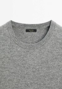 Pull gris clair à col rond avec une texture en maille fine et une étiquette de marque noire cousue à l'intérieur du col.