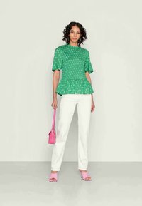 Blusa peplum verde com padrão floral branco, mangas curtas volumosas, usada com calças brancas. Acessórios incluem uma mala rosa e saltos a condizer.