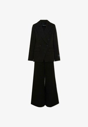 Blazer noir à double boutonnage avec larges revers, assorti d'un pantalon taille haute à jambes larges sur fond blanc.