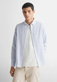 Lichtblauw button-up shirt met lange mouwen, kraaghals, met een gladde textuur. Gemaakt over een eenvoudig wit t-shirt, gecombineerd met lichtgekleurde broek.