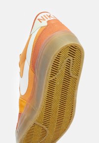 Sneaker Nike con una tomaia in suede arancione, swoosh bianco e suola in gomma traslucida con motivo a zigzag.