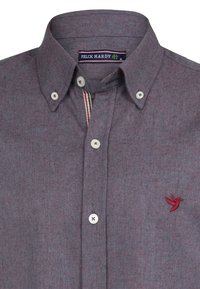 Camisa gris de botonadura con una tela texturizada, presenta botones blancos y un logotipo de ave bordado en rojo en el lado izquierdo del pecho.