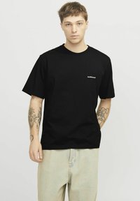 Sort bomulds T-shirt med korte ærmer og rund hals, forsynet med et lille hvidt logo på venstre brystområde og en glat tekstur.