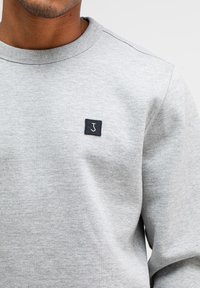 Grijs sweatshirt gemaakt van een katoenmix. Heeft een geribbelde ronde hals en een klein zwart vierkant label met een wit logo op de borst.