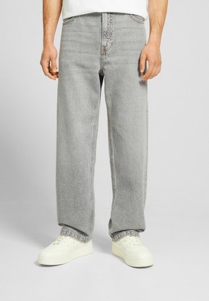 Vaqueros holgados de color gris claro, confeccionados en denim, con una textura desgastada, diseño tradicional de cinco bolsillos y costuras cosidas. Combinados con zapatillas blancas.