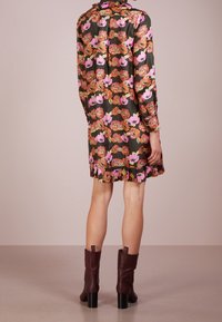 Abito a maniche lunghe di colore verde scuro con motivi floreali in arancione e rosa. Presenta un colletto e un orlo plissettato. Abbinato a stivali con tacco marroni.