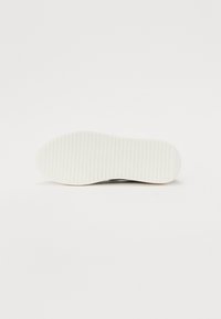 Semelle de chaussure blanche avec des stries visibles, texture lisse, forme ronde et design léger. Aucun logo ou motif distinctif noté.