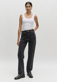 Zwarte denim rechte jeans met een hoge taille, voorzien van voorzakken en contrasterende stiksels. Gecombineerd met een fitted witte tanktop.