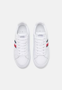 Białe skórzane sneakersy z płaskimi sznurowadłami, z czerwono-niebieskim paskiem po boku i logo "Tommy Hilfiger" na języku.