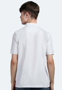 Polo bianco con colletto e maniche corte, realizzato in tessuto testurizzato, con dettagli cuciti sulle spalle e sulle cuciture laterali.