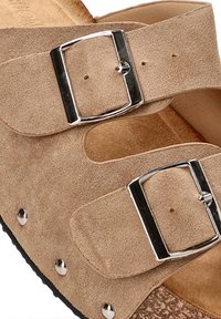 Sandalia de ante beige con dos correas ajustables, hebillas plateadas y una plantilla de corcho. Presenta pequeños tachuelas metálicas en el borde de la suela.