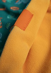 Fleece stof i strålende orange med en tekstureret overflade; har en glat grøn foring med små blad- og etikette mønstre.