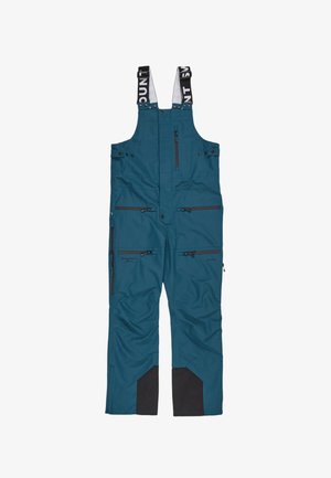 Teal winter overalls with adjustable straps, multiple zippered pockets, and black reinforced patches at the ankles. Smooth texture and durable material.