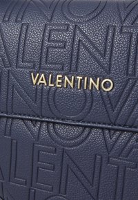 Sac en cuir texturé bleu marine avec un motif « VALENTINO » emboss�é, rehaussé de ferrures dorées et de coutures visibles le long des coutures.