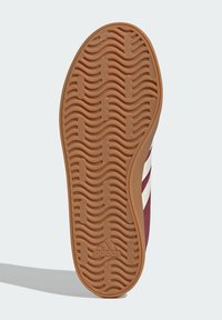 Sole obuvi s vlnitým dezénem, tan gumový materiál, logo Adidas v blízkosti paty, vínová svrchní část s bílými pruhy viditelnými na boku.