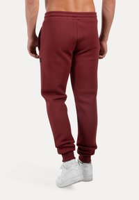 Pantalones deportivos burdeos de tejido suave con una cinturilla elástica, piernas ajustadas y bolsillos laterales. Combinados con zapatillas blancas.
