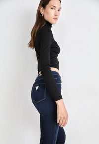 Čierny dlhý rukáv s rolákom skombinovaný s tmavomodrými vysokými džínsami s trojuholníkovými vreckami a zlatými švami.