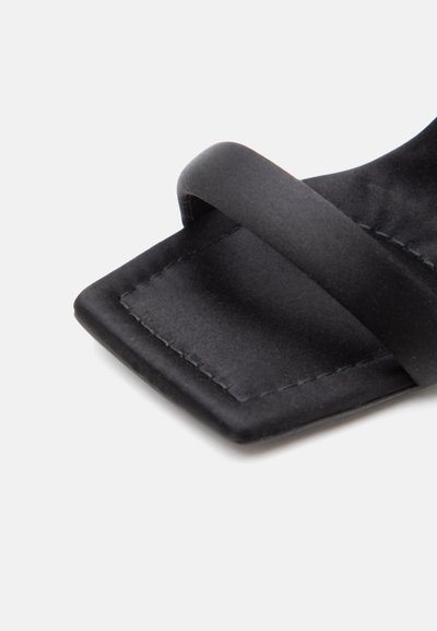 Μαύρο σανδάλι με τετράγωνη μύτη και ένα φαρδύ λουράκι πάνω από τα δάχτυλα, με εμφανείς ραφές και ματ φινίρισμα.