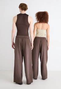 Braunfarbiger Tank-Top und beiges trägerloses Oberteil kombiniert mit lockeren braunen Hosen, die einen elastischen Bund und eine glatte Textur aufweisen.