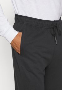 Pantaloni sportivi neri con una vita elasticizzata, dettaglio con coulisse e tasche laterali. Il materiale è morbido e liscio. I dettagli includono cuciture lungo le cuciture.