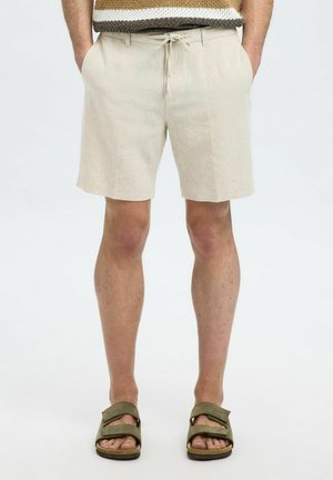 Beige Leinen-Shorts mit einem Kordelzugbund, Fronttaschen und einem lockeren Schnitt, kombiniert mit olivgrünen Sandalen mit einem Riemen-Design.