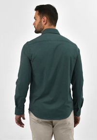 Donkergroene longsleeve met kraag, knoopmanchetten, een gladde textuur en een aansluitend design, van achter bekeken.