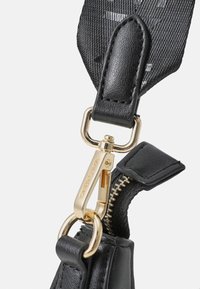Svart lærreim med gullmaskiner, med et klips og glidelåsdetaljer, teksturert overflate, og en del av stoffreimen med detaljer.