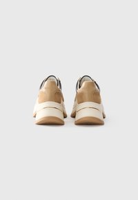 Pair of beige and white sneakers with chunky soles viewed from the back against a plain light background.