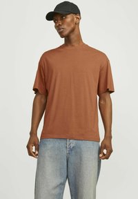 Brun kortærmet t-shirt lavet af bomuld, med rund hals og afslappet pasform, parret med lyseblå denimjeans og en sort cap.