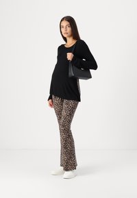 Svart langermet topp med rund hals, kombinert med brune leopardmønstrede flared leggings. Hvite joggesko og en svart håndveske fullfører antrekket.