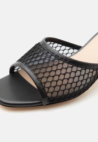 Μαύρο σανδάλι slide με ανοιχτό δάχτυλο και φαρδιά λωρίδα από δίχτυ με εξαγωνικό σχέδιο και δερμάτινη επένδυση.