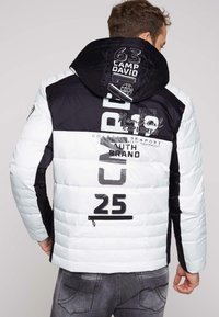 Giacca imbottita con un tema di colori bianco e nero, dotata di cappuccio, stampe grafiche e dettagli con zip sulla schiena.