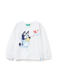 Una camicia bianca a maniche lunghe con un personaggio di cartone animato di un cane con pelo blu, un muso giallo e cuori rossi. Il tessuto ha una consistenza morbida.